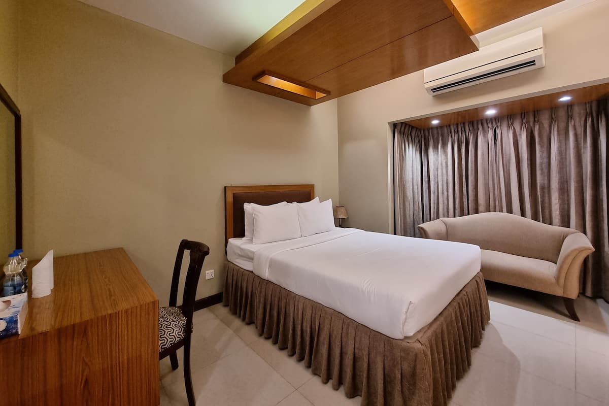 Habitación de hotel con cama, escritorio, silla, sofá, aire acondicionado y ventana con cortinas.