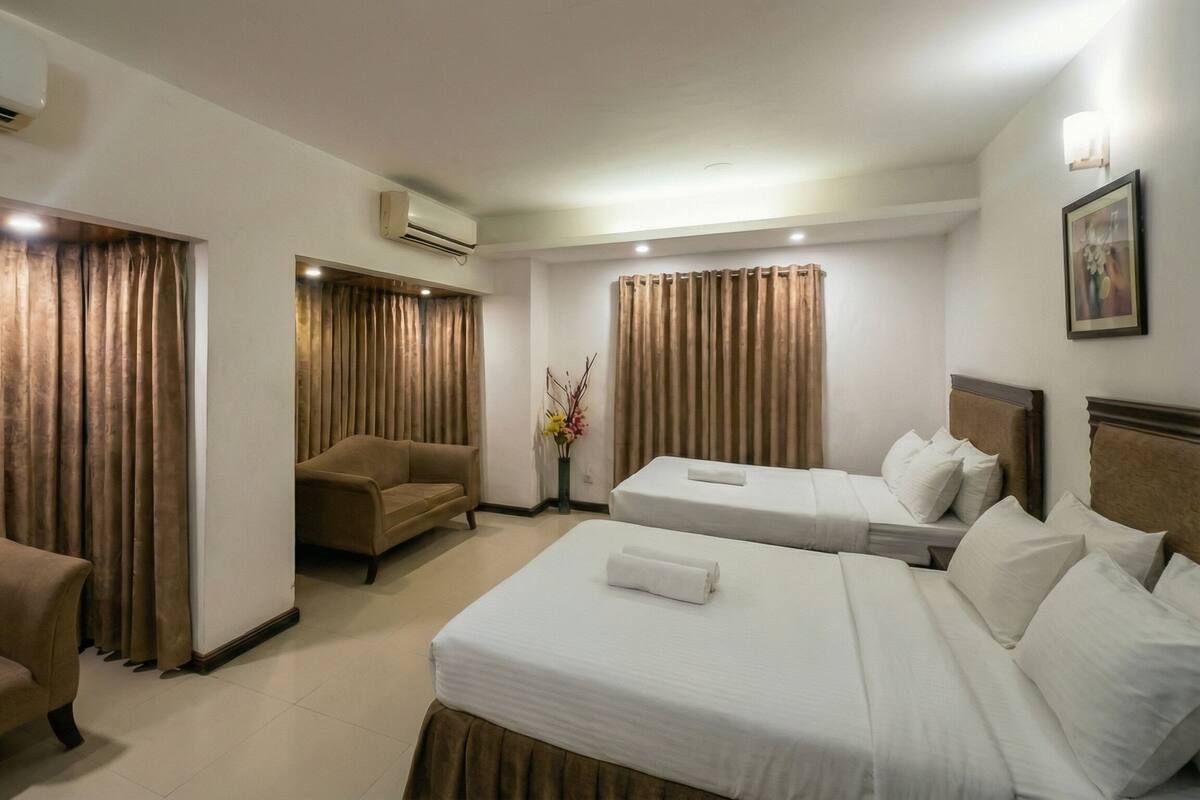 Habitación de hotel con sofá, dos camas individuales, una silla y equipo de aire acondicionado.