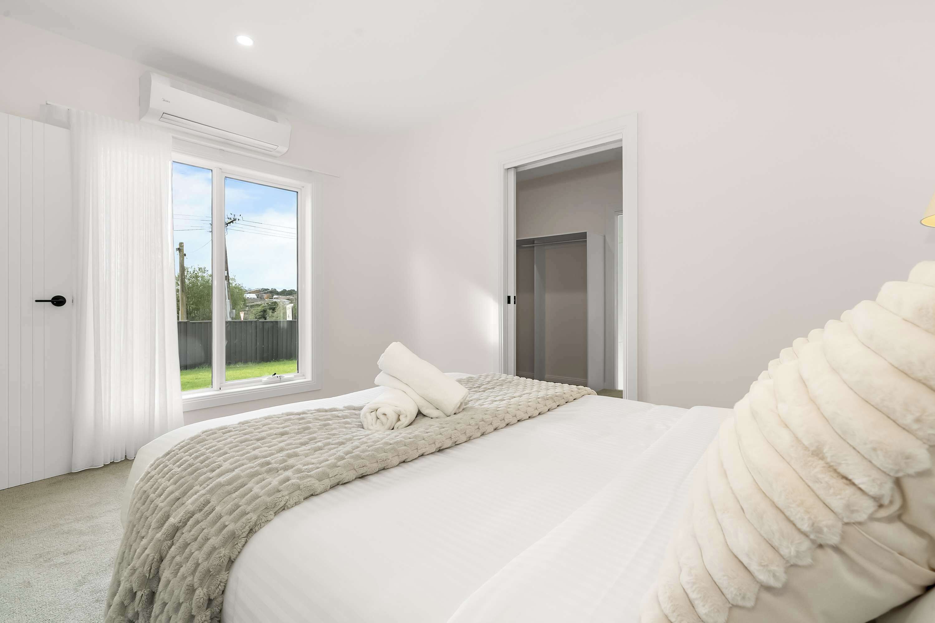 A bedroom with a bed, a window, an air conditioning unit, and a door.