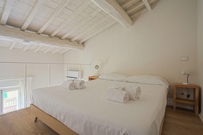 A bedroom with a large bed, wooden beams on the ceiling, a nightstand, and a bedside table with a lamp. - Loft Libertà No2 (Florence)