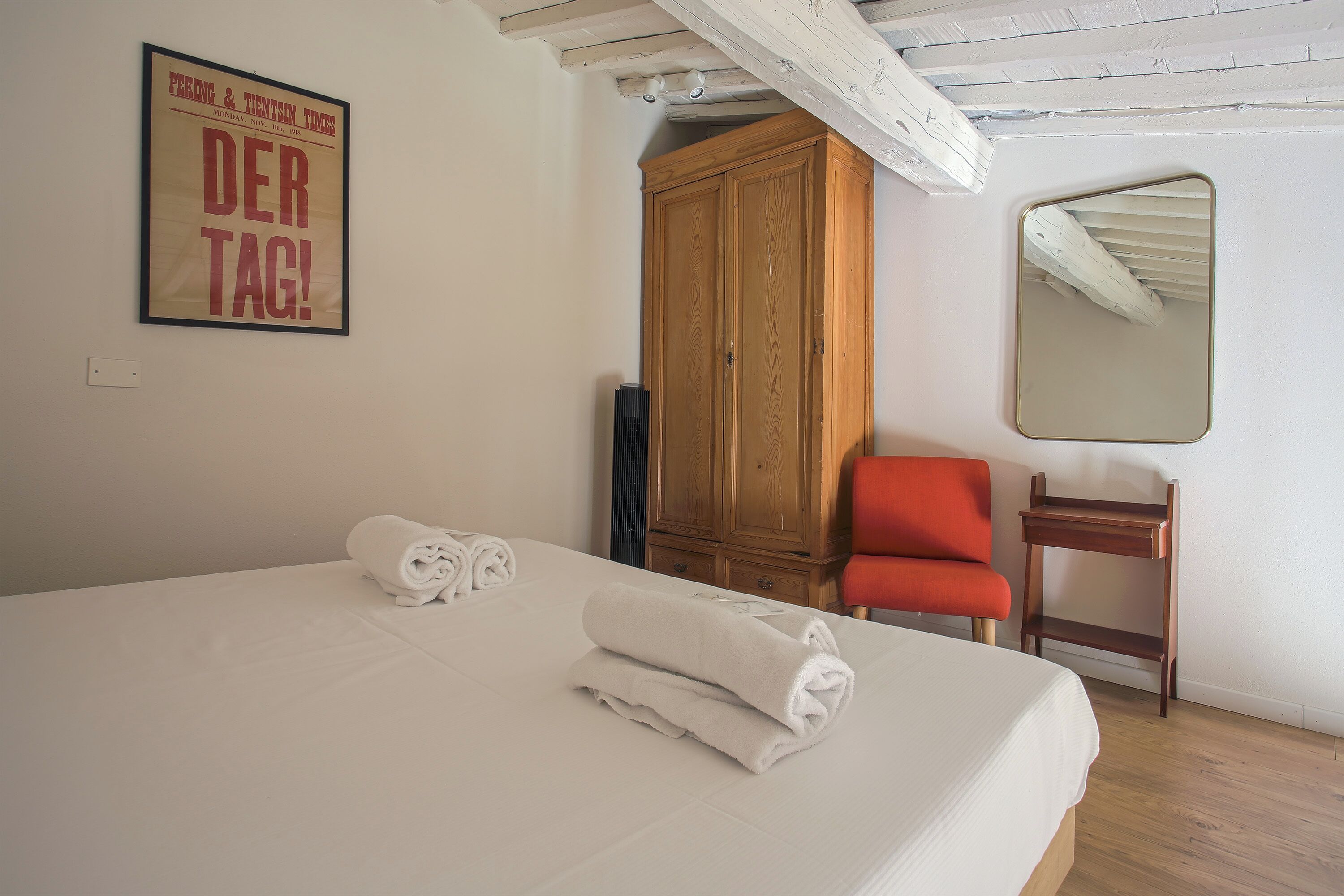 Une chambre à coucher avec un lit, une armoire en bois, une chaise rouge, une petite table et un miroir au mur.