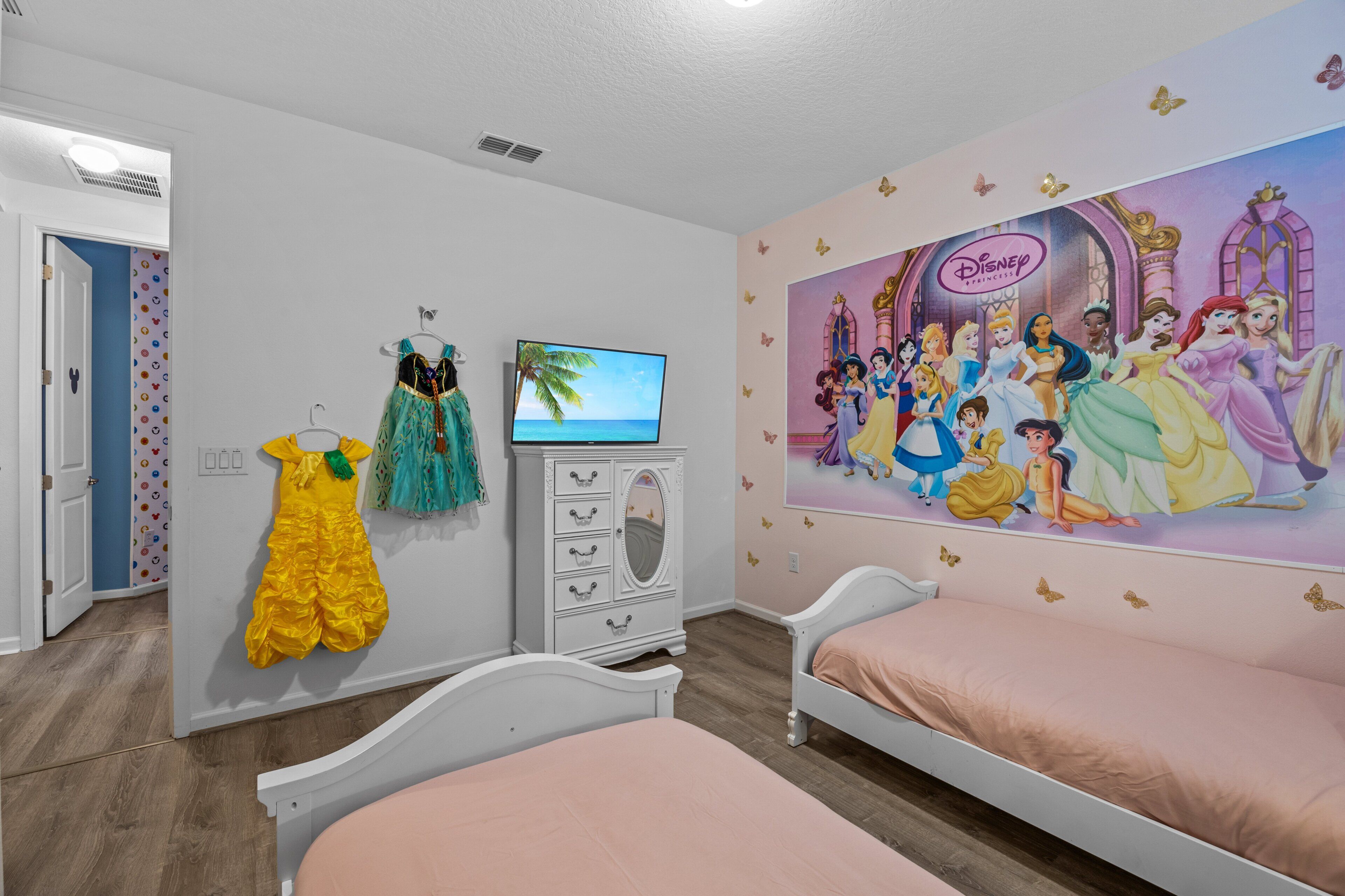 Camera da letto con un letto, una cassettiera, una TV e un murale a tema Disney.