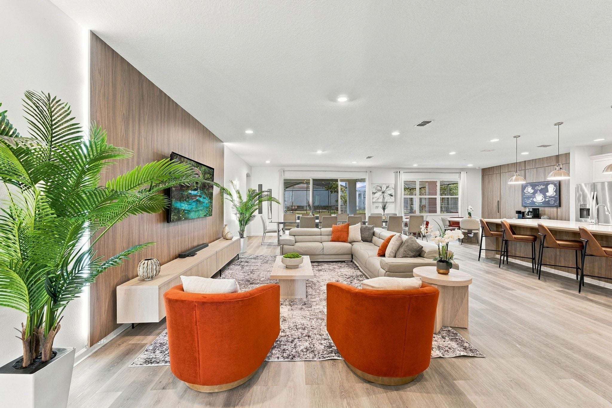 Un salon moderne avec un canapé, des fauteuils orange, une table basse et un téléviseur fixé au mur.