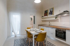 A modern kitchen with white cabinets, a built-in oven, and a dining area with a white table and yellow chairs. - Ai Benedettini Apartment by Wonderful Italy (Catania)