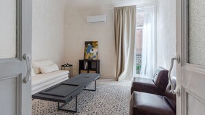 Um quarto com sofá, mesa, estante e janela com cortinas.