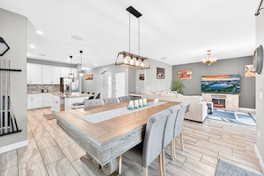 A modern kitchen with a large island, a dining area with a wooden table and chairs, a living room with a sofa and TV, and a fireplace. - Sol117-5484-6-pg - Solterra's Dream Home (Davenport)