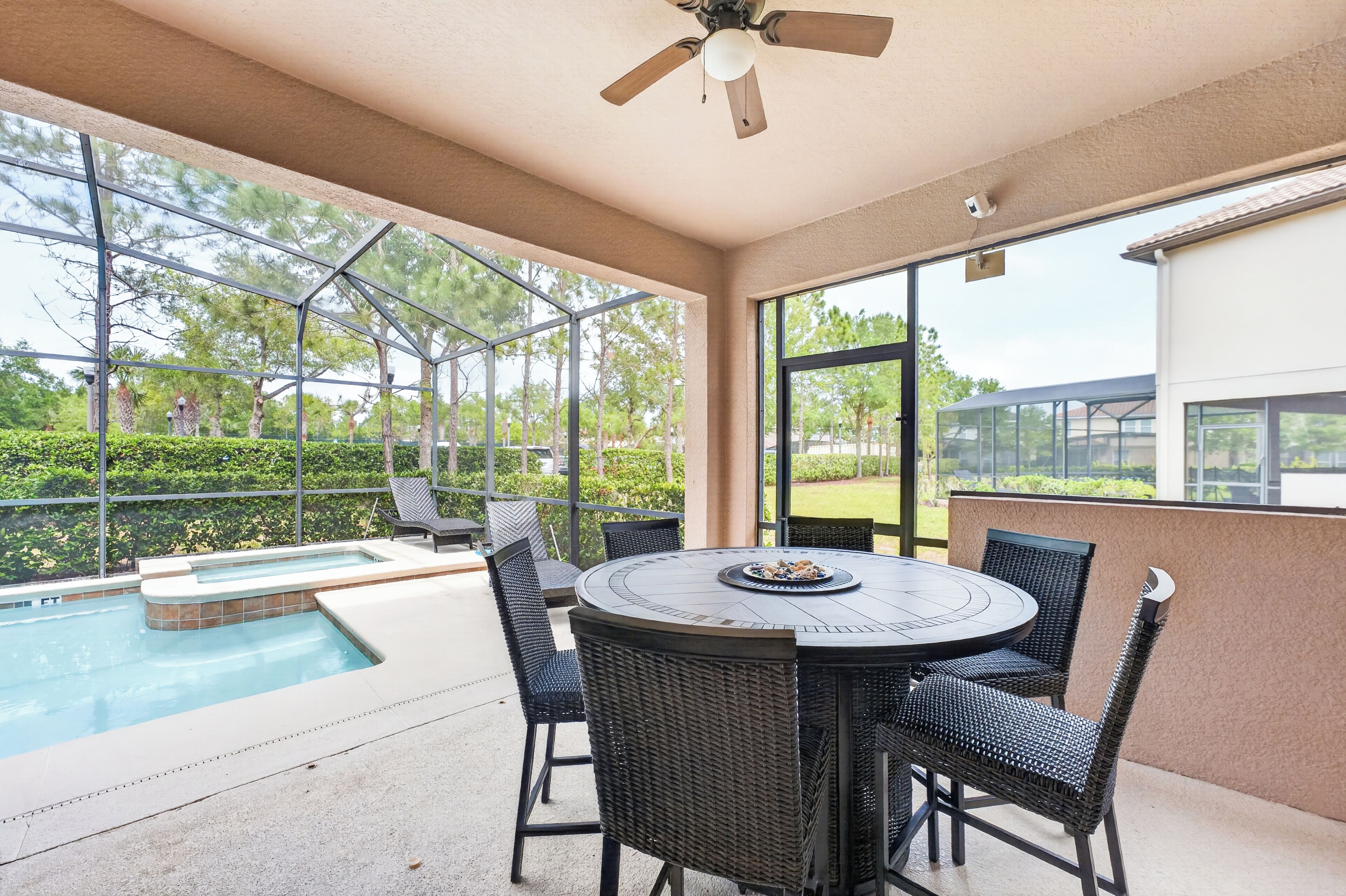 A covered outdoor area with a pool, a round table with chairs, and a ceiling fan.