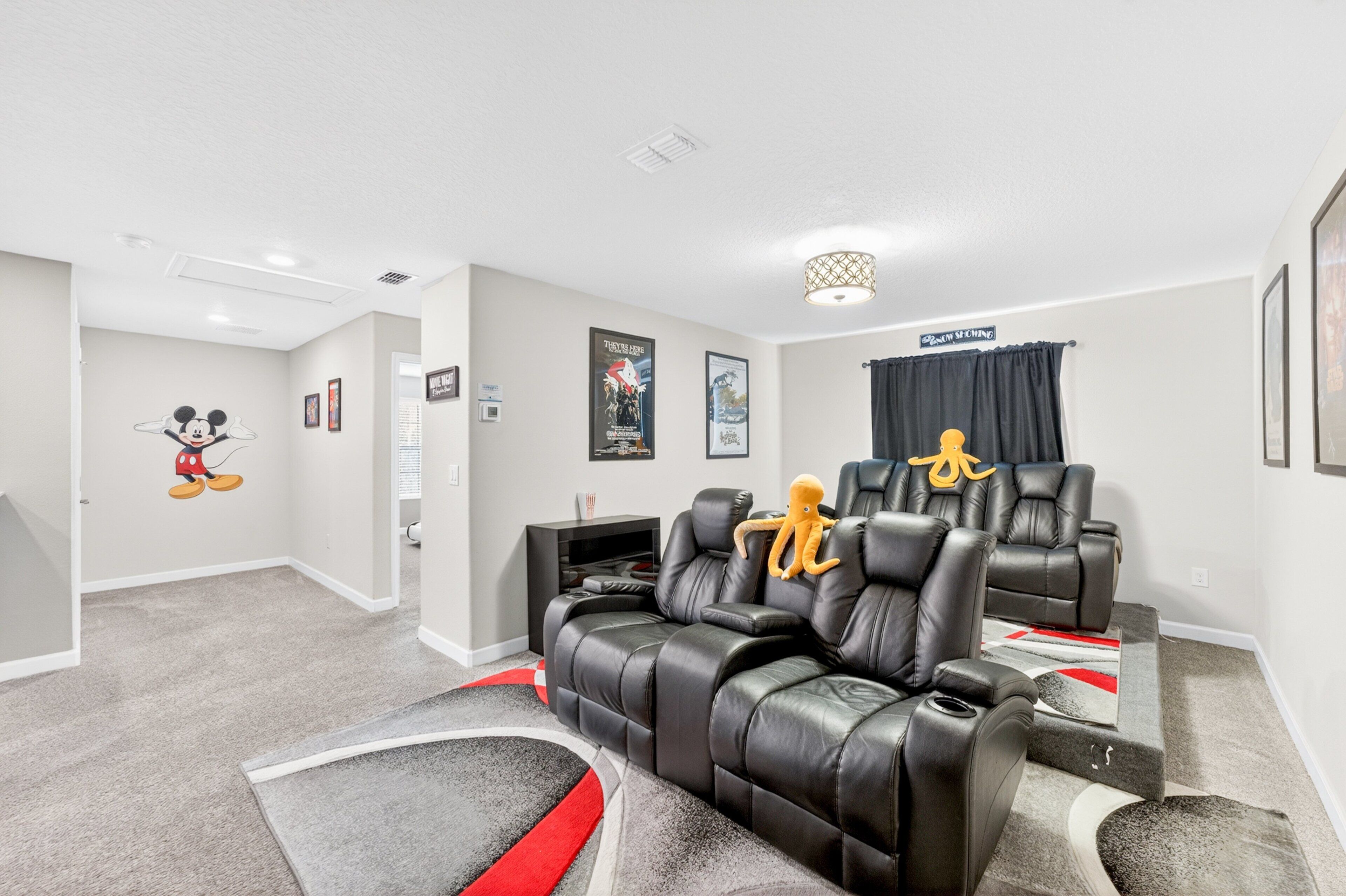 A home theater room with a large screen, two leather recliners, a small table, and a carpeted floor.