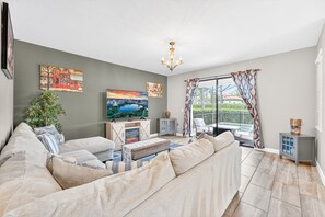 A living room with a sofa, TV, fireplace, and a balcony with a view. - Sol117-5484-6-pg - Solterra's Dream Home (Davenport)