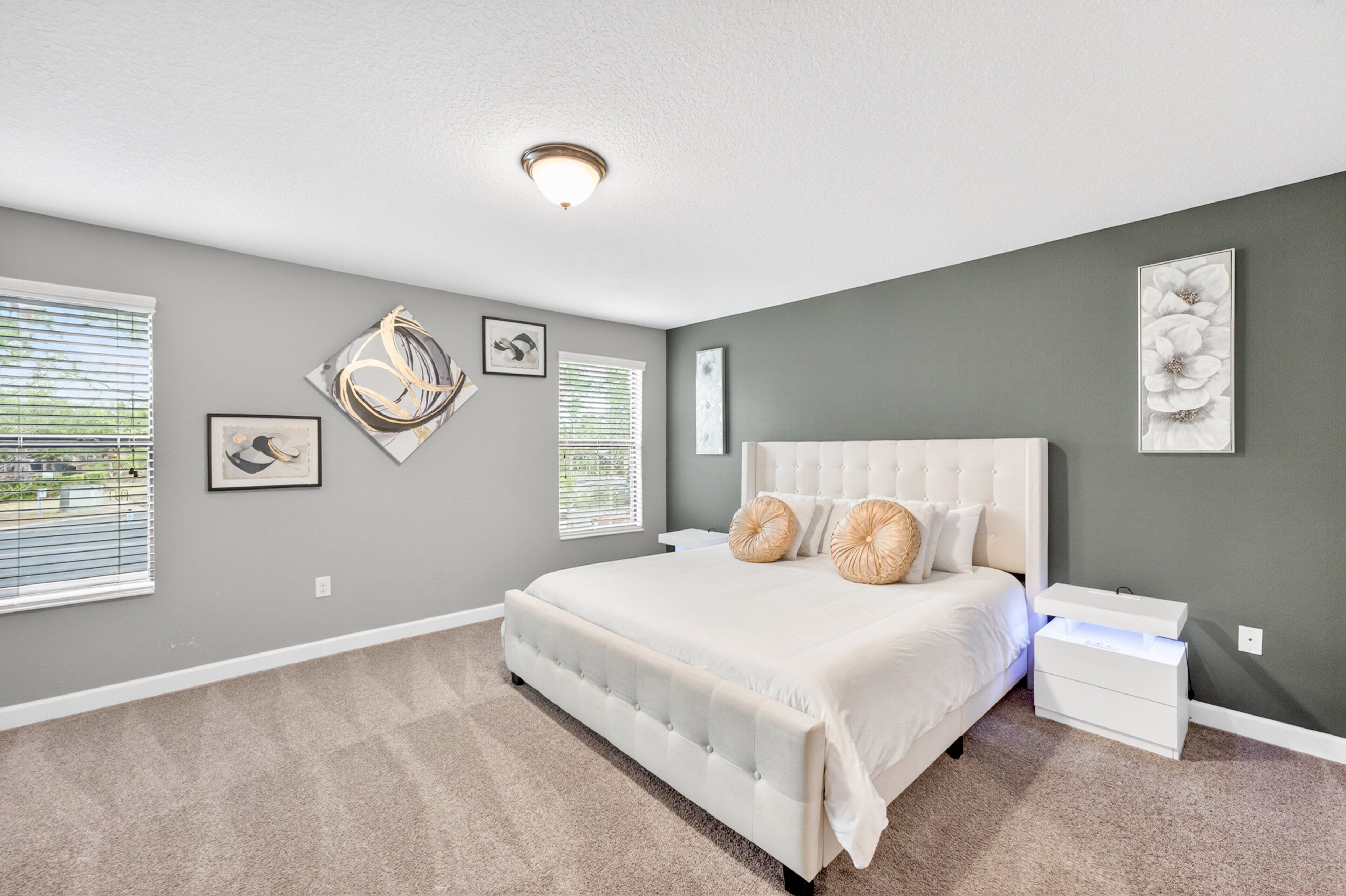 A bedroom with a large bed, a nightstand, a wall-mounted lamp, and artwork on the walls.