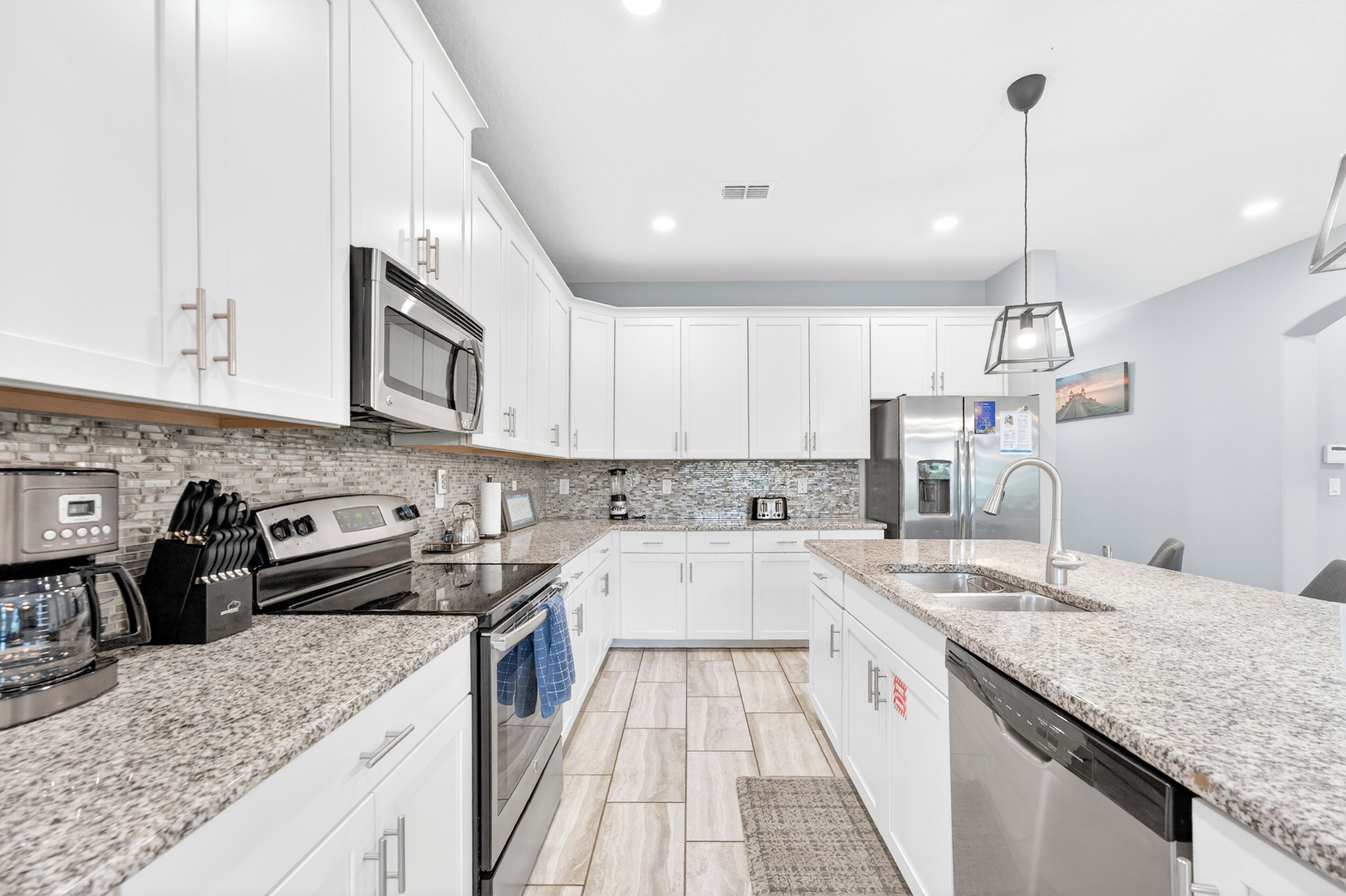 A modern kitchen with white cabinets, granite countertops, stainless steel appliances, and a central island.