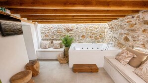 Un baño con paredes de piedra, una bañera, un banco de madera y un sofá blanco con cojines estampados.