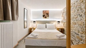 Un dormitorio con cama, mesitas de noche, un radiador, una pared de piedra y un cuadro enmarcado en la pared.