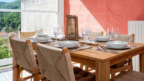 Mesa de comedor dispuesta con platos, vasos y una cesta tejida, con vistas a un paisaje pintoresco.