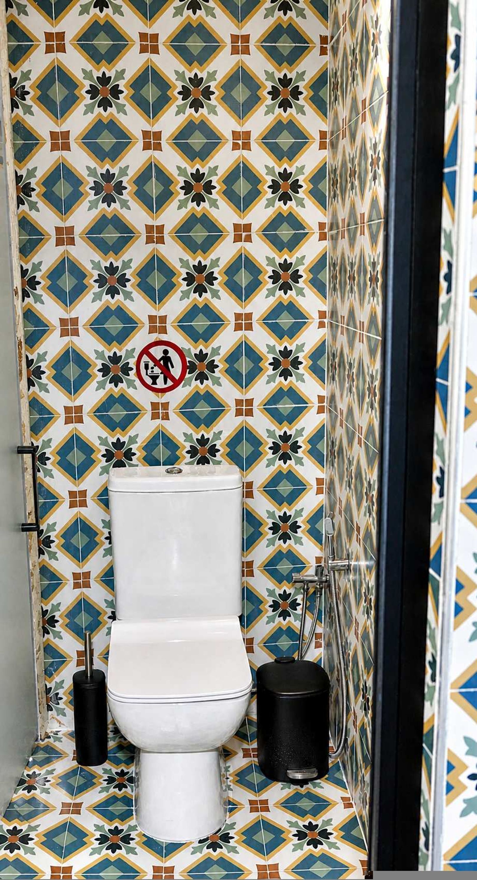 Une salle de bain avec un mur recouvert de carreaux à motifs, des toilettes, un bidet et une poubelle.