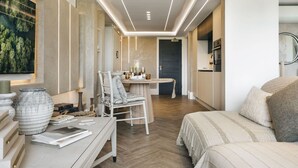 A modern hotel room with a wooden floor, a dining area with a table and chairs, a bed with a striped bedspread, and a large window with a view of trees. - The Hide Ridgestone (Penrith)