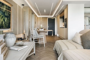 A modern hotel room with a wooden floor, a dining area with a table and chairs, a bed with a striped bedspread, and a large window with a view of trees. - The Hide Ridgestone (Penrith)