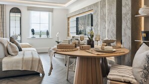 A modern living room with a round wooden table, a sofa, and a large window with a view. - The Hide Ridgestone (Penrith)