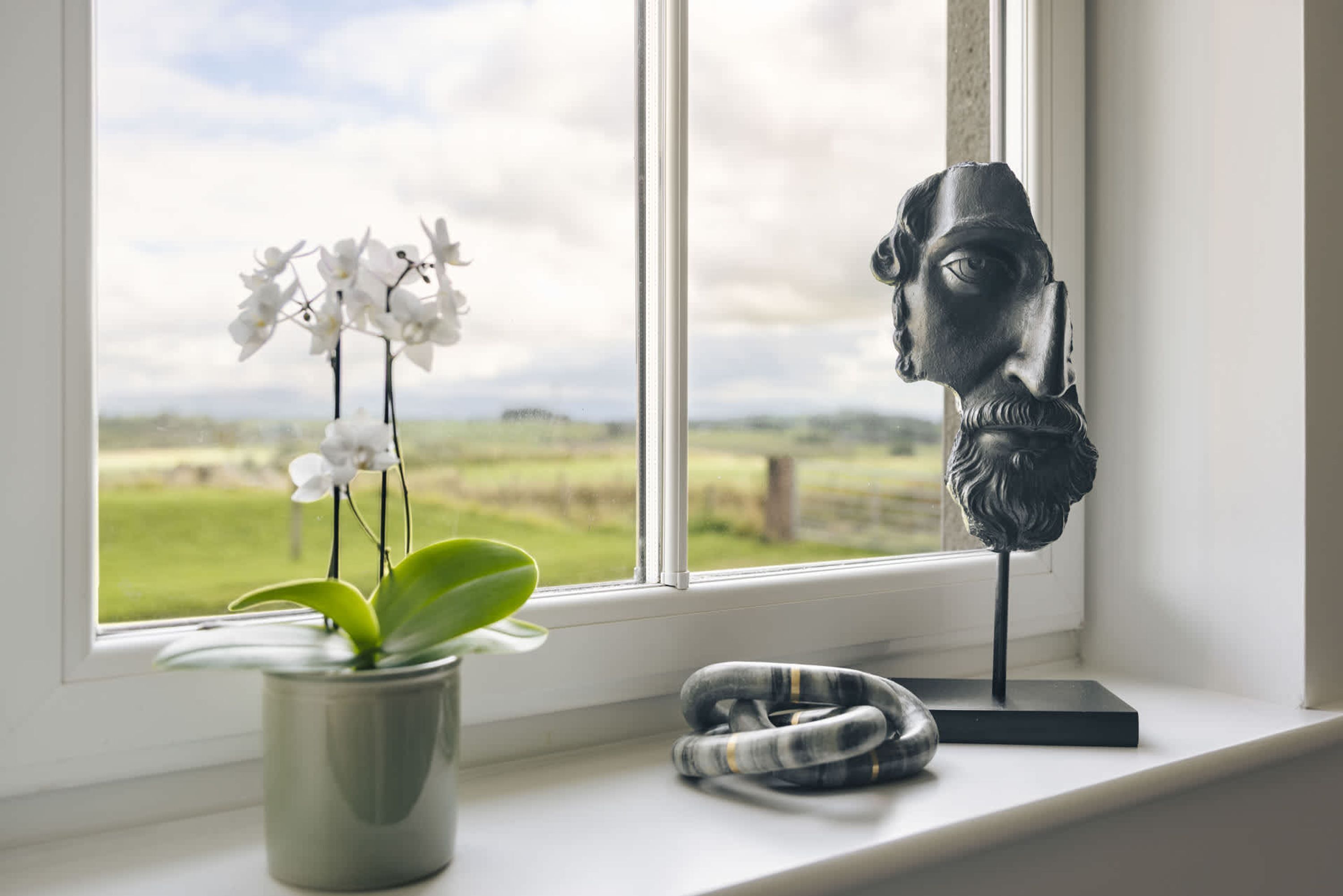Una ventana con vista a un campo, una planta en maceta y una escultura en el alféizar.