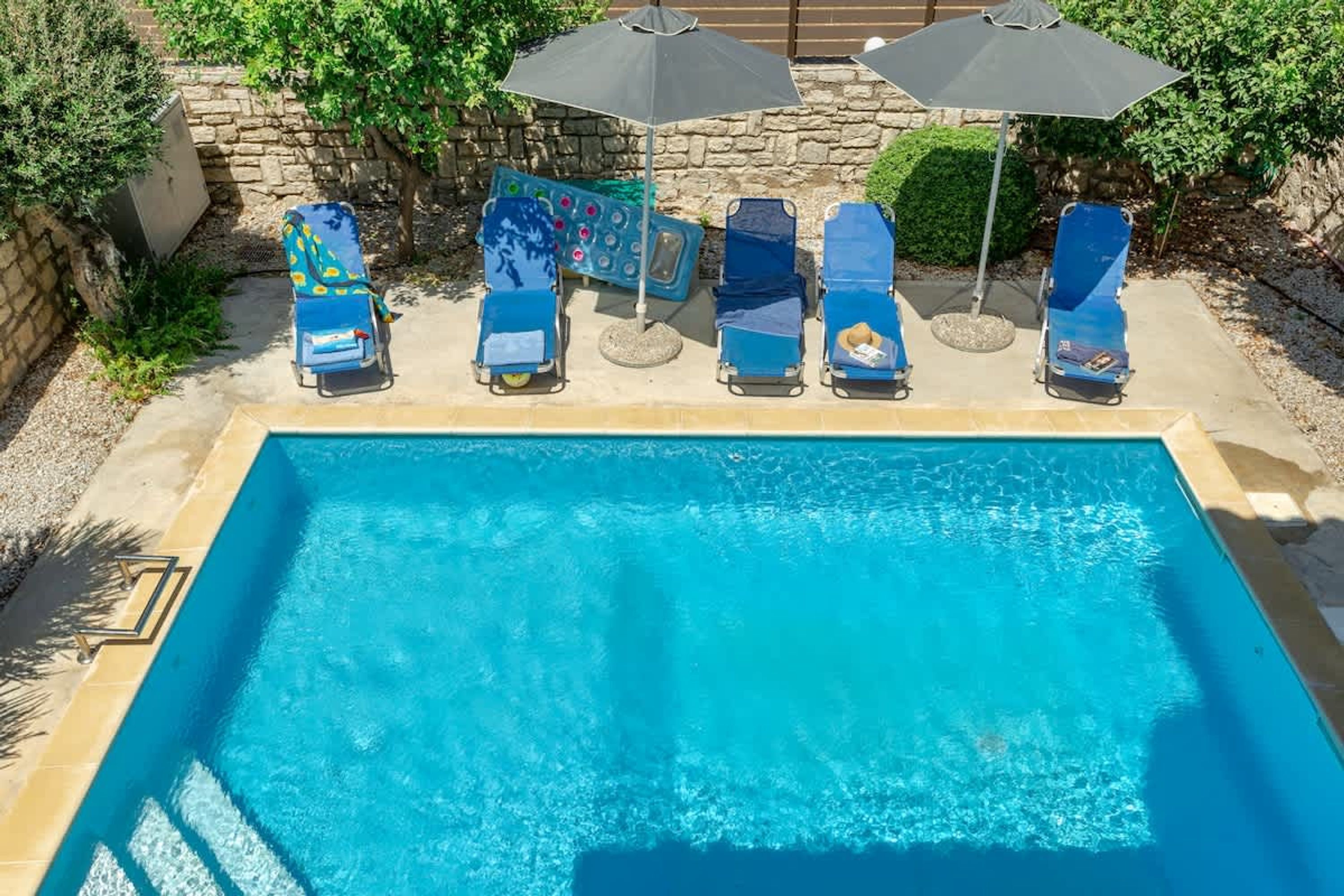 A rectangular swimming pool with six lounge chairs and two umbrellas.
