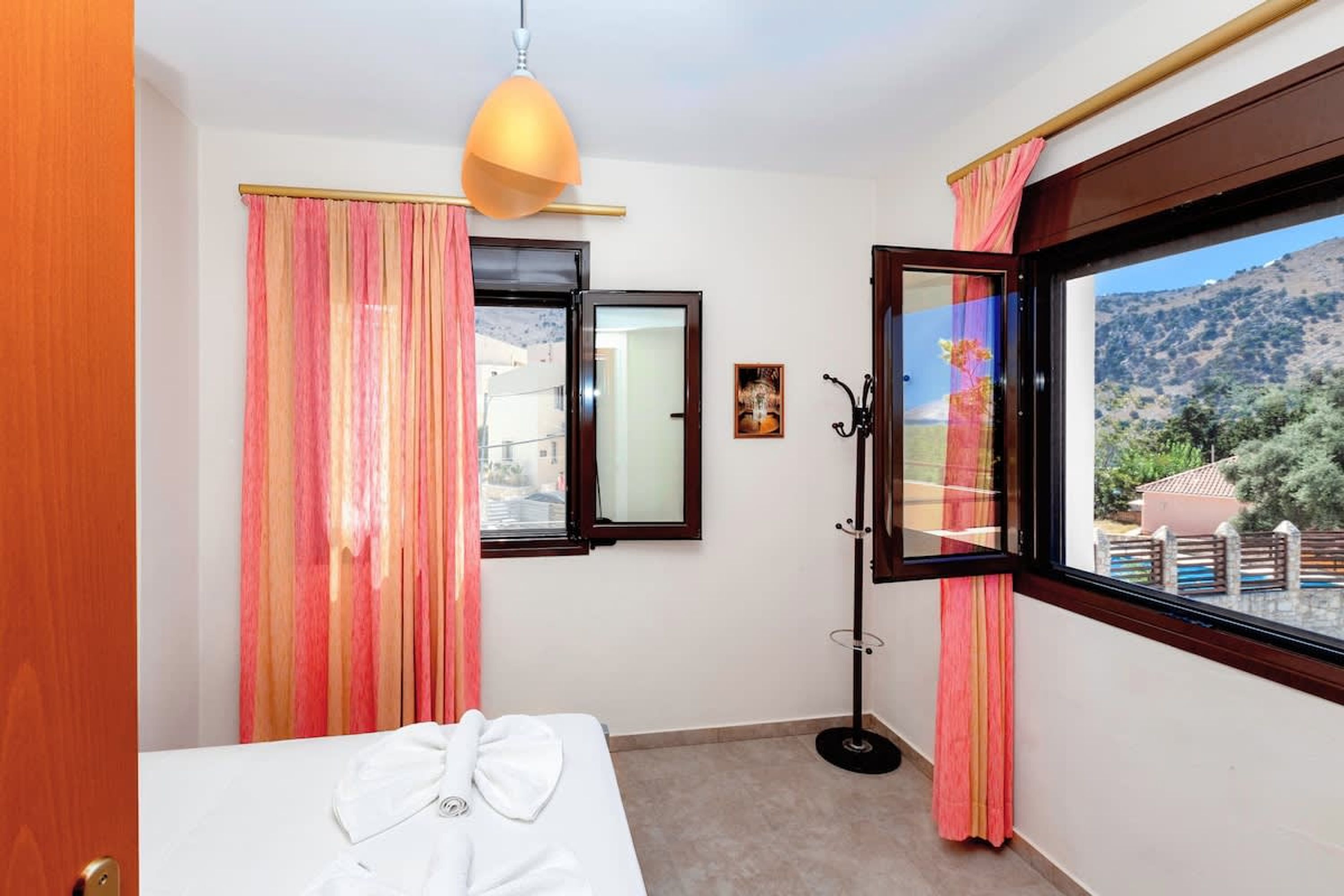 Ein Hotelzimmer mit Bett, einem Vorhangfenster, einer Stehlampe und Blick auf eine Berglandschaft.