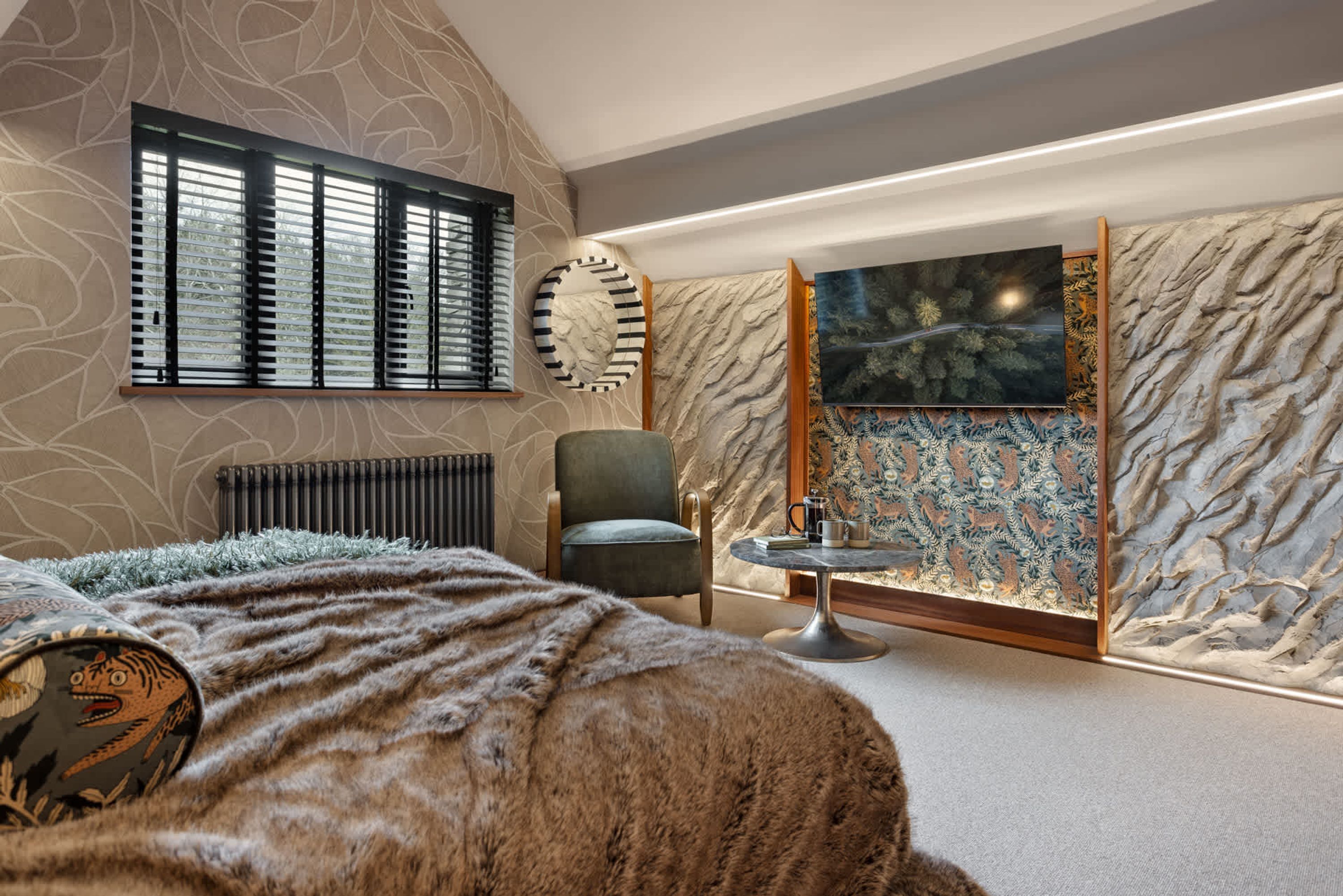 A bedroom with a bed, a chair, a table, and a wall with a painting.