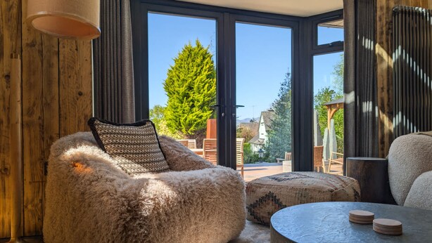 A cozy room with a plush, furry chair, a round table with coasters, and a view through large glass doors to the outdoors. - Wyke View Ridgestone (Windermere)