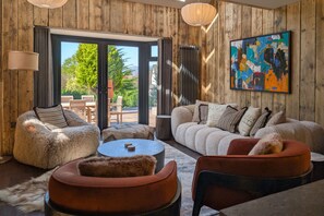 A modern living room with a wooden interior, a large window, and a colorful abstract painting. - Wyke View Ridgestone (Windermere)