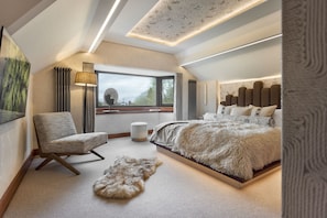 Un dormitorio con una cama grande, una silla, un ventanal y una lámpara en el techo.