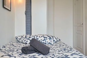 A neatly made bed with patterned bedding, a rolled towel, and a wall-mounted light fixture. - Bel Appartement 2 Chambres Avec Espace Travail (Lille)