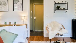 A room with a bed, a chair, a shelf with plants, and a door leading to another room. - Bel Appartement 2 Chambres Avec Espace Travail (Lille)