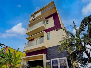 A multi-story building with balconies, a garage, and surrounding tropical vegetation. - Collection O New Theni Bus Terminal (Theni)