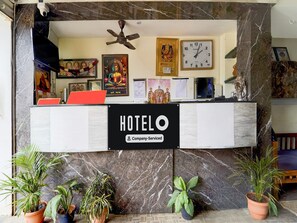 A hotel reception desk with a 'HOTELO' sign, a clock, and various religious posters on the wall. - Collection O New Theni Bus Terminal (Theni)