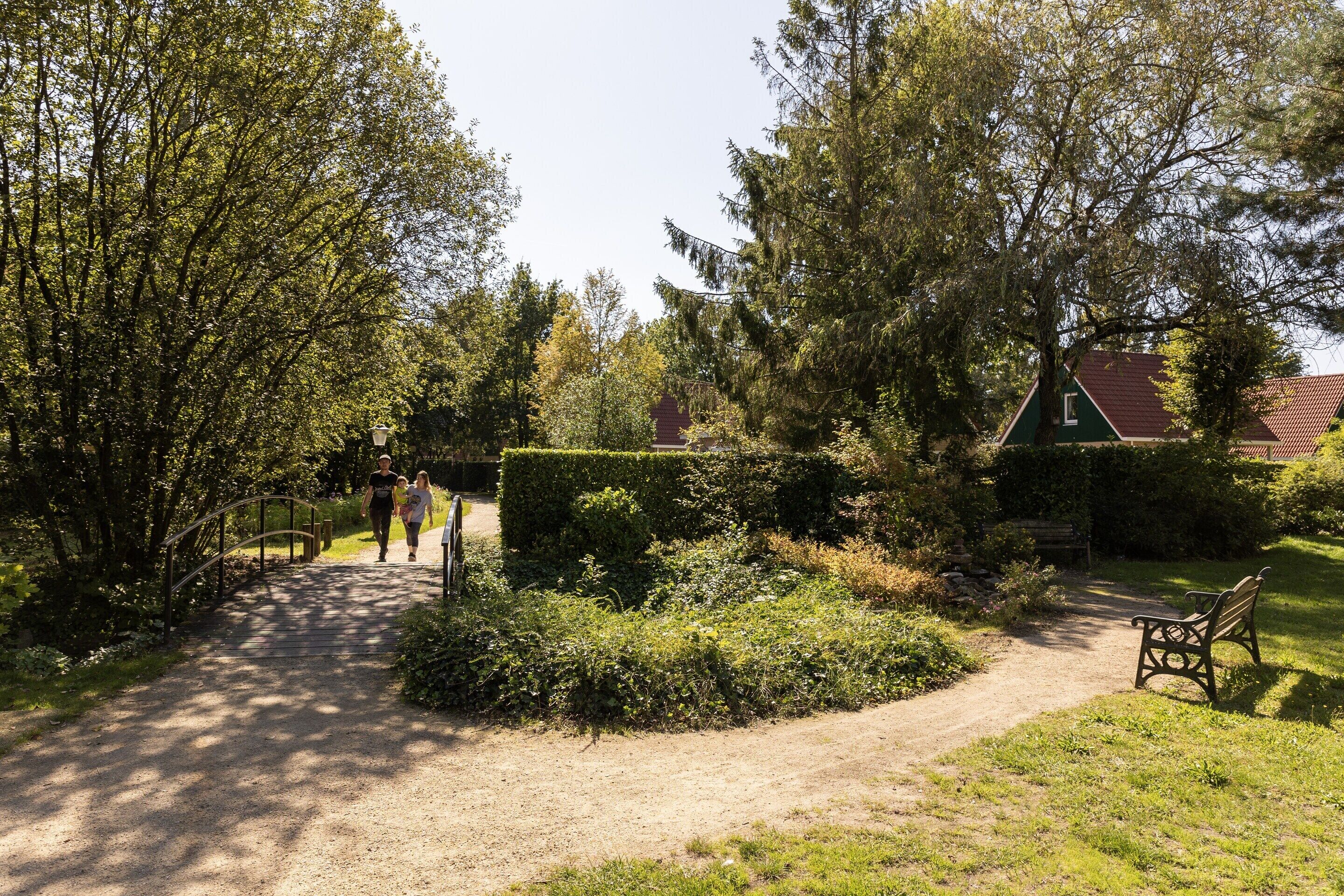 A garden pathway leading to a building with a green roof, surrounded by trees and a bench.
