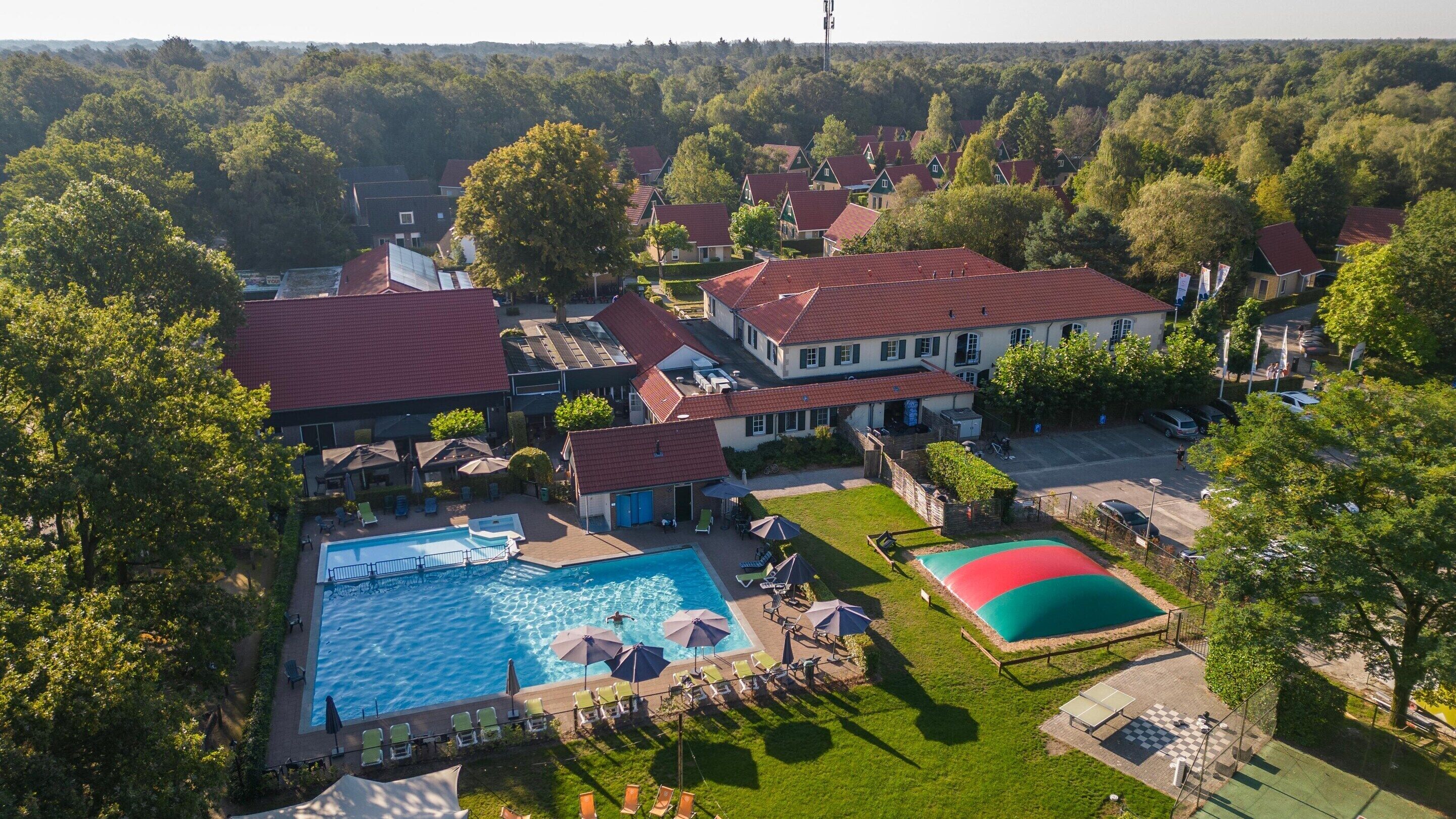 An aerial view of a residential area with a swimming pool, a tennis court, and houses with red roofs.