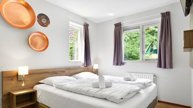 A bedroom with a wooden headboard, a bed with white linens, two wall-mounted clocks, and a window with curtains. - Holiday Home With Sauna, 18 km. From Tilburg (Diessen)