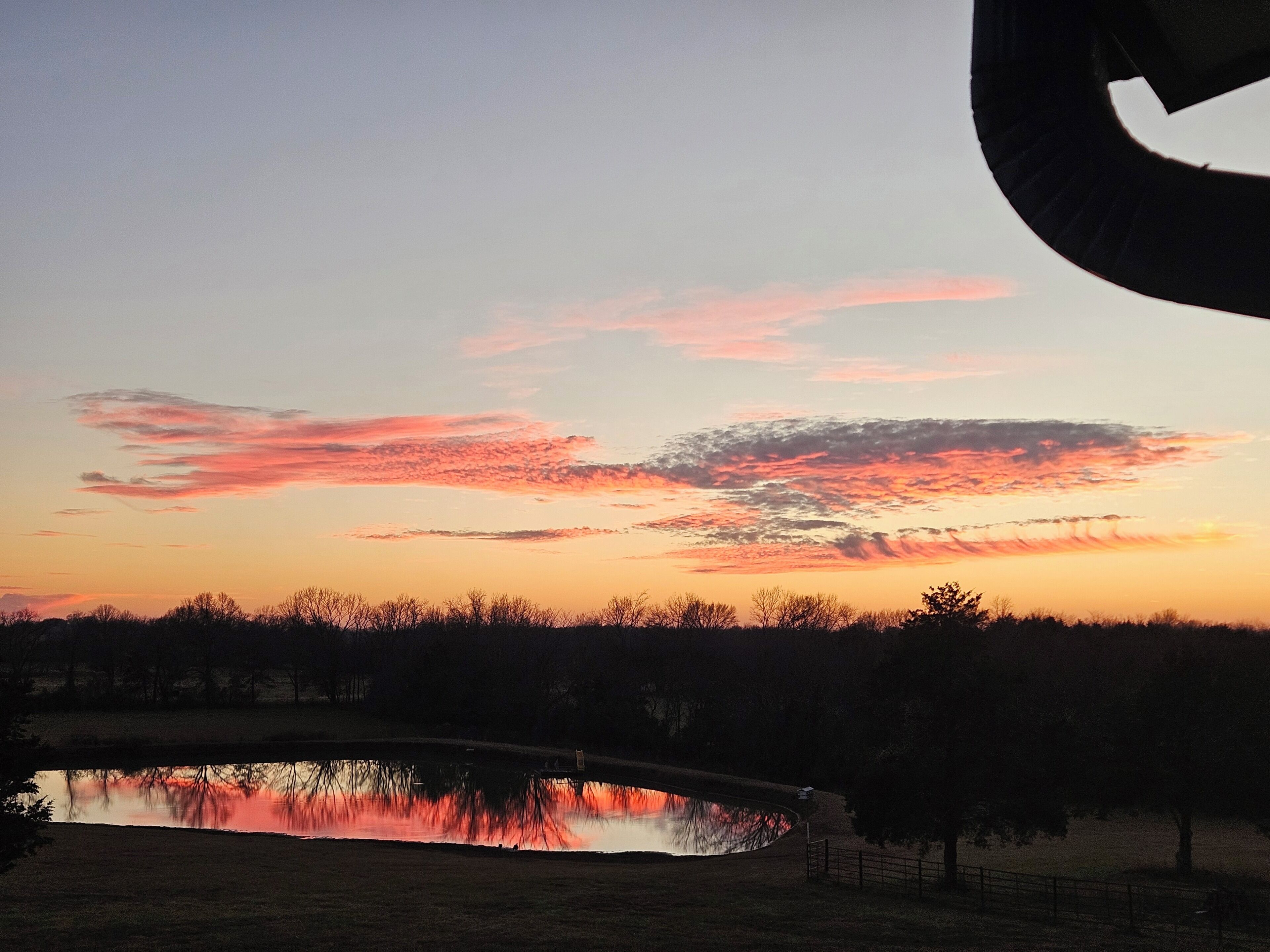 A sunset over a calm lake with a bridge in the foreground.