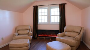 A room with two leather armchairs, a wooden ottoman, and a fireplace with a fire. - Private Country Suite Near Truman Lake & Fishing (Clinton)