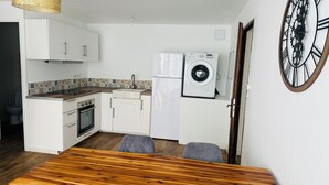 Een kleine keuken met een wasmachine, een eettafel en een grote wandklok.