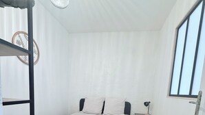 Een stapelbed met een gestreept dekbedovertrek, een nachtkastje, een lamp en een raam met jaloezieën.