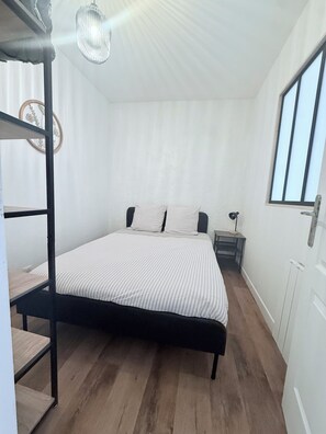 Een stapelbed met een gestreept dekbedovertrek, een nachtkastje, een lamp en een raam met jaloezieën.