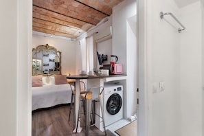 A compact room with a bed, a washing machine, a small table with chairs, a mirror, and a shower area. - Apartment 'Termini Suite Roma' with Wi-Fi and Air Conditioning (Roma)