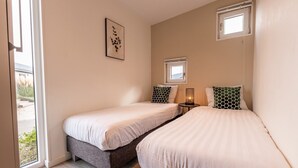 Un dormitorio con dos camas, una mesita de noche con lámpara, una ventana y un cuadro en la pared.