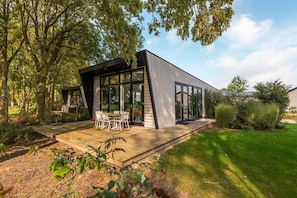 Una casa moderna con una terraza, ventanas grandes y un jardín.