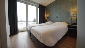 Ein Schlafzimmer mit zwei Betten, einem großen Fenster und Blick auf ein Gewässer.