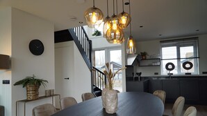 Eine moderne Küche mit Essbereich, inklusive rundem Tisch, Stühlen, Pendelleuchten und einer Treppe.