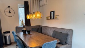 Un comedor moderno con una mesa de madera, sillas azules, un sofá gris, lámparas colgantes y un estante con adornos.
