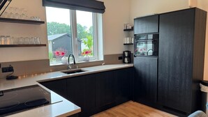 Una cocina moderna con armarios oscuros, horno empotrado, lavamanos y una ventana con vistas a zonas verdes.