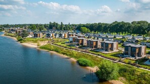 Et boligområde med moderne huse langs en flodbred, med en blanding af et- og flereetages bygninger, og et frit udsyn til floden.