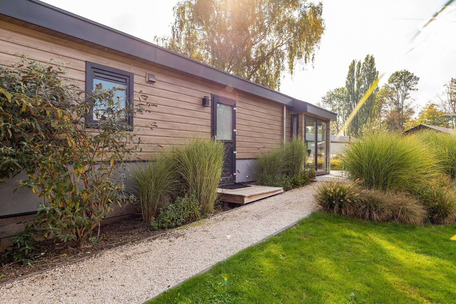 Ein modernes Haus mit einem Kiesweg, der zum Eingang führt, umgeben von verschiedenen Pflanzen und Bäumen.